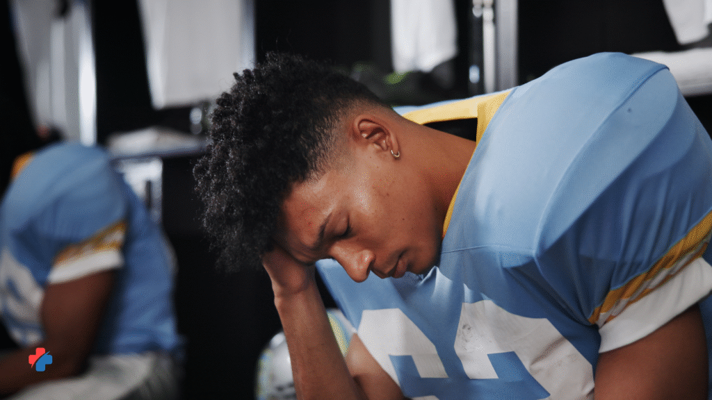 image of football player in locker room holding his head demonstrating one of the key signs of a concussion
