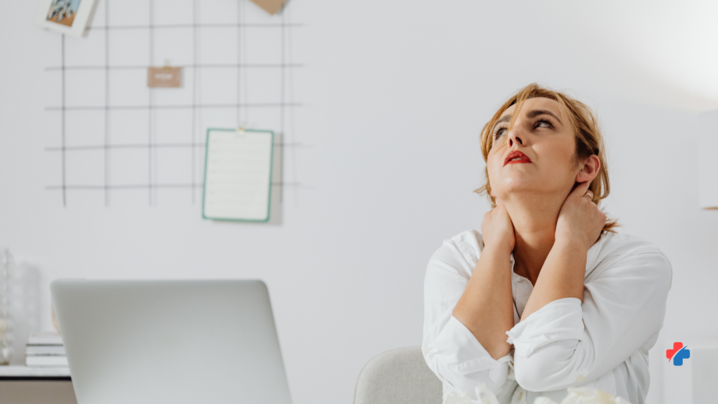 Stressed woman at a laptop holding her neck—effects of chronic stress such as muscle tension, poor sleep, and fatigue that can raise illness risk.